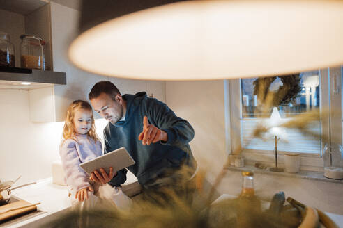 Father sharing tablet PC with daughter in kitchen - MOEF04485