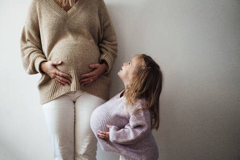 Daughter imitating mother's pregnancy in front of wall - MOEF04489