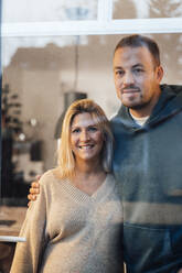 Couple standing with arm around seen through glass - MOEF04490