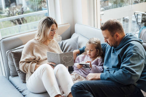 Eltern teilen Ultraschalluntersuchung mit Tochter, die zu Hause auf dem Sofa sitzt - MOEF04498