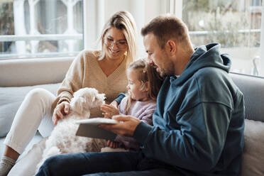 Daughter petting dog sitting by parents at home - MOEF04499
