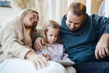 Vater betrachtet Mädchen, das zu Hause von der Mutter mit einem Tablet-PC bedient wird - MOEF04504