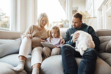 Girl using tablet PC sitting by parents and dog at home - MOEF04505