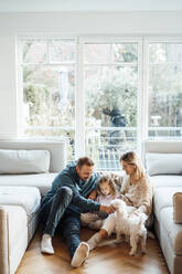 Smiling family with dog sitting on ground at home - MOEF04509