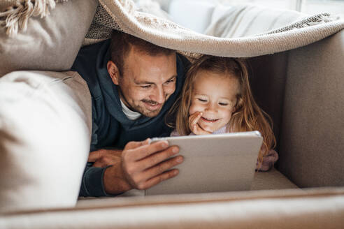 Glücklicher Vater und Tochter benutzen einen Tablet-PC unter einer Decke zu Hause - MOEF04513