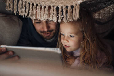Father sharing tablet PC with daughter under blanket at home - MOEF04514