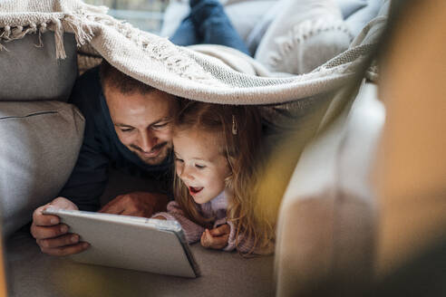 Glückliches Mädchen, das mit seinem Vater zu Hause einen Tablet-PC betrachtet - MOEF04516