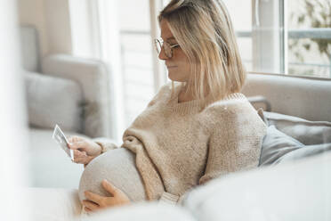 Woman with blond hair holding ultrasound photo at home - MOEF04525