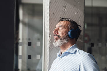 Businessman with eyes closed wearing wireless headphones - JOSEF17956