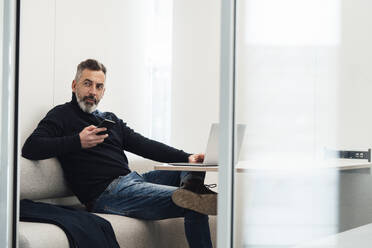 Businessman sitting with smart phone and laptop in office - JOSEF17981