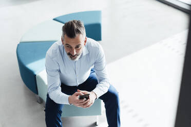 Thoughtful businessman sitting with smart phone on seat - JOSEF18002