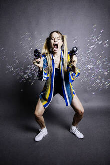 Woman shooting bubbles with guns against gray background - JATF01350