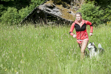 Young woman jogging with dog in field - HHF05830