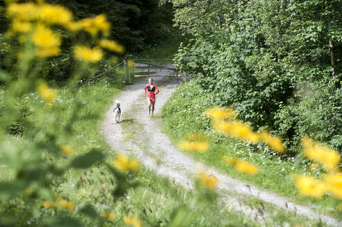 Dog and woman jogging on narrow path - HHF05834