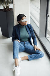 Junge Geschäftsfrau mit Virtual-Reality-Headset sitzt im Büro - JOSEF18020