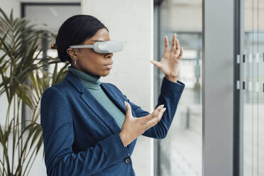 Geschäftsfrau mit Virtual-Reality-Headset gestikuliert im Büro - JOSEF18026