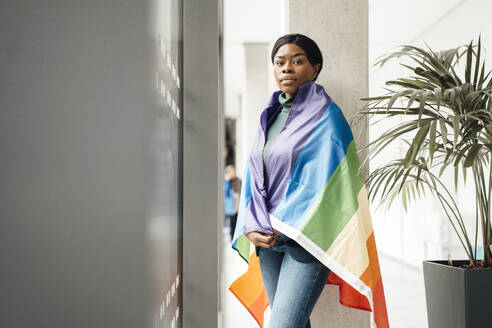 Young businesswoman wrapped in rainbow flag standing at office - JOSEF18030