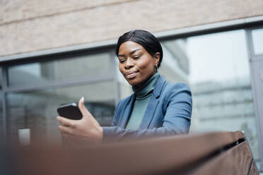 Lächelnde Geschäftsfrau, die mit ihrem Smartphone vor dem Büro im Internet surft - JOSEF18089