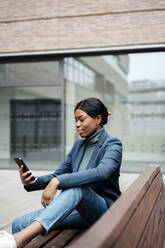 Geschäftsfrau mit Smartphone auf einer Bank sitzend - JOSEF18090