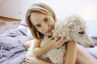 Lächelnde nackte Frau, die einen Pudelhund zu Hause umarmt - JATF01366