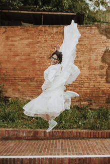 Glückliche Frau im Hochzeitskleid springt auf den Fußweg - GMLF01338