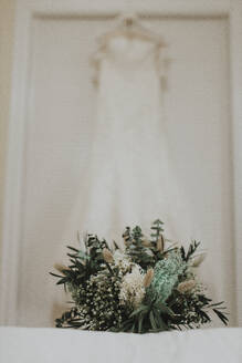 Brautstrauß auf Bett mit Hochzeitskleid im Hintergrund - GMLF01342