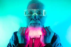 Positiv bärtiger älterer männlicher Hipster mit Brille, der in die Kamera schaut, mit Neonlicht unter dem Gesicht im Studio - ADSF43490