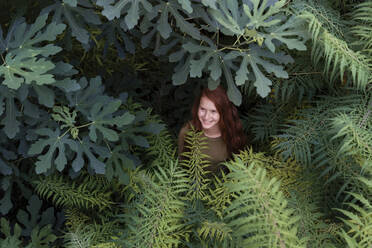 Lächelndes Mädchen, das inmitten von Pflanzen in der Natur steht - AAZF00234