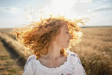 Glückliche rothaarige Frau, die sich die Haare im Feld wirft - AAZF00241