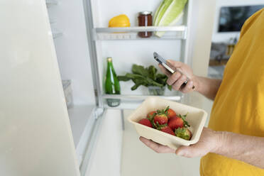 Senior man holding fresh strawberries and smart phone at home - SVKF01366