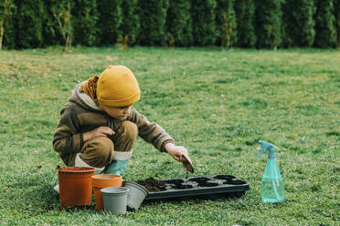 Junge, der im Garten hockend Erde in einen Behälter gibt - VSNF00645