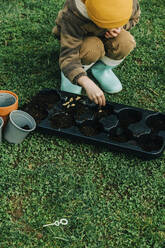 Boy putting zucchini seeds in container at garden - VSNF00646