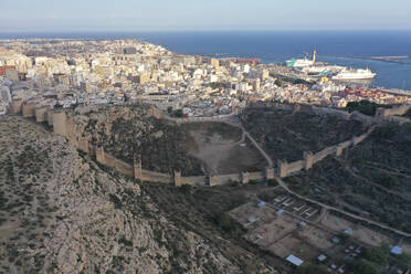 Luftaufnahme einer Festung mit einer Mauer, die beide Seiten des Tals verbindet, der Muralla de Jairán mit der Stadt im Hintergrund in Almeria, Andalusien, Spanien. - AAEF17702