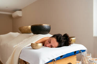 Entspannte Frau, die eine alternative Therapie mit Klangschalen erhält, während sie auf einem Bett im Wellness-Salon liegt - ADSF43540