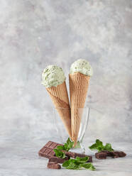 Leckere Eiskugeln in Waffeltüten mit frischer Minze und Schokolade in Glasvase vor grauem Hintergrund - ADSF43548