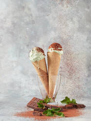 Leckere Eiskugeln in Waffeltüten mit frischer Minze und Schokolade in Glasvase vor grauem Hintergrund - ADSF43549