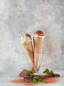 Leckere Eiskugeln in Waffeltüten mit frischer Minze und Schokolade in Glasvase vor grauem Hintergrund - ADSF43549