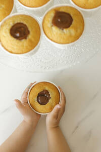 Hand eines Mädchens hält gesalzenen Karamell-Cupcake auf dem Tisch - VIVF00454