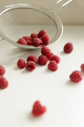 Raspberries spilled from colander on table - VIVF00455