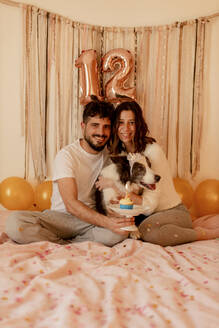 Ein glücklicher Mann und eine glückliche Frau feiern den Geburtstag ihres Border Collie Hundes zu Hause - GMLF01363