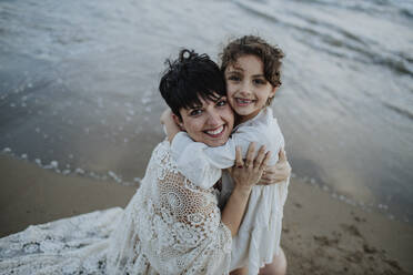 Glückliches Mädchen, das seine Mutter am Strand umarmt - GMLF01380