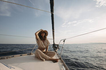 Lächelnde Frau mit Hut auf einem Segelboot sitzend - GMLF01382