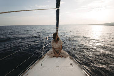 Woman sitting on sailboat and enjoying vacation at sunset - GMLF01383