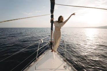 Smiling woman with arm raised enjoying on sailboat - GMLF01386