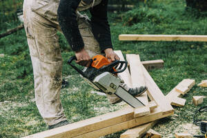 Zimmermann schneidet Holz mit Kettensäge auf Gras - VSNF00649