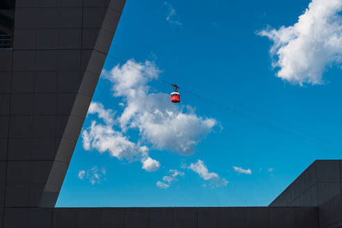 Low Winkel der hellen Seilbahn Kabine gegen blauen bewölkten Himmel über zeitgenössischen mehrstöckigen Gebäuden - ADSF43600