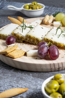 Appetitlicher Käse serviert auf einem Holztisch mit reifen Weintrauben und Crackern, dekoriert mit Rosmarinzweigen neben Oliven in Schalen auf dem Tisch - ADSF43611