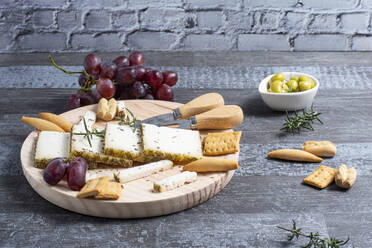 Appetitlicher Käse serviert auf einem Holztisch mit reifen Weintrauben und Crackern, dekoriert mit Rosmarinzweigen neben Oliven in Schalen auf dem Tisch - ADSF43612