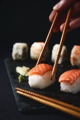 Unbekannte Person isst köstliche, appetitliche Sushi mit Lachsfilet, die mit Stäbchen auf das Brett gelegt werden - ADSF43631