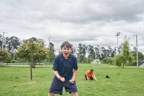 Fröhlicher Jugendlicher in Sportkleidung, der ein erfolgreiches Spiel während des Trainings auf dem Fußballplatz feiert - ADSF43645